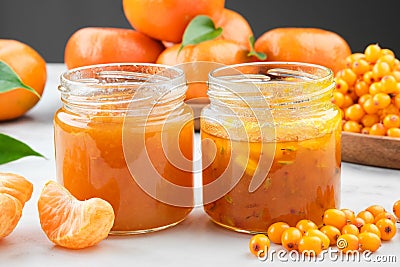 Jars of sea buckthorn and tangerine jam. Plate of sea buckthorn berries and mandarin oranges fruits on background Stock Photo