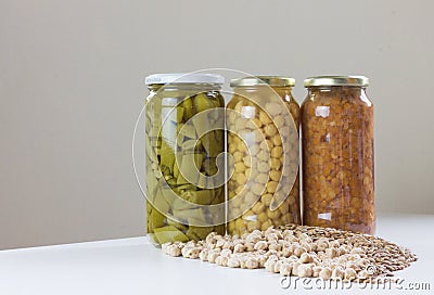 Jars of non-perishable chickpeas, lentils, and green beans with spilled seeds on the table Stock Photo