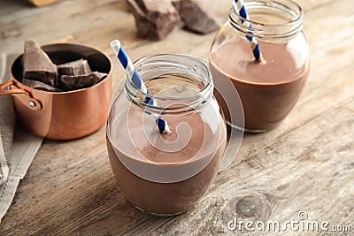 Jars with tasty chocolate milk on wooden table. Stock Photo