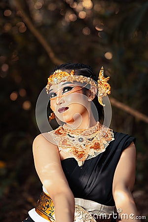 Javanese woman with golden crown and black costume chilling inside the forest while wearing makeup Stock Photo