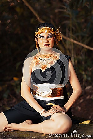 Javanese woman with golden crown and black costume chilling inside the forest while wearing makeup Stock Photo