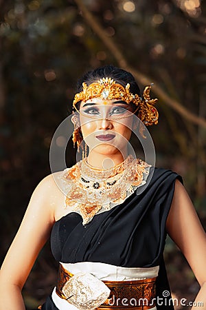 Javanese woman with golden crown and black costume chilling inside the forest while wearing makeup Stock Photo