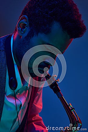 Jazz in modern music. Close up photo of young handsome man playing saxophone in neon light. Gel portraits. Stock Photo