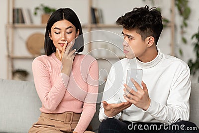 Jealous Chinese Husband Showing Cheating Wife Her Cellphone At Home Stock Photo