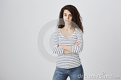 Jealous girlfriend being suspicious. Indoor shot of beautiful curly-haired caucasian girl standing with crossed hands Stock Photo
