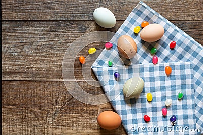 Jelly beans and colored eggs with blue and white gingham towel on wood background Cartoon Illustration