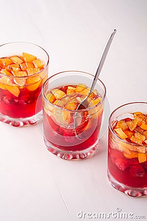 Jelly dessert with fruits apricot raspberry in three drinking glasses with single spoon yellow red summer white background in row Stock Photo