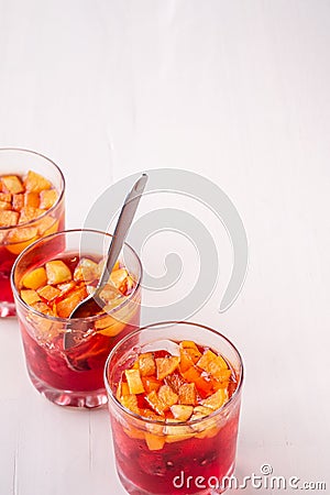 Jelly dessert with fruits apricot raspberry in three drinking glasses with single spoon yellow red summer white background in row Stock Photo