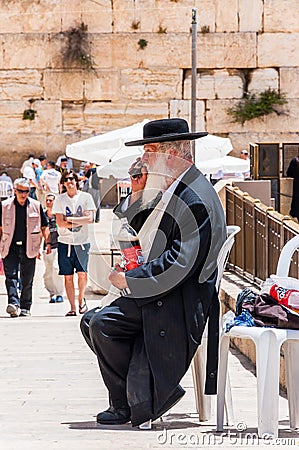 Jewish orthodox in black suit and hat sitting and drinking near the entrance alley to the Western Wall. People, locals and Editorial Stock Photo