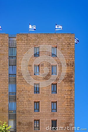 Jerusalem Israel 12-052019 View of a tall stone building with windows and balconies and Israeli flags on the roof, from the side, Editorial Stock Photo