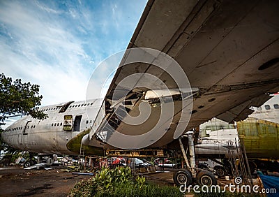 Jetliner Being Cut To Pieces For Recyling Purpose at Airplane Graveyard Under The Blue Cloudy Sky. Under Wing Part Being Dismantle Stock Photo