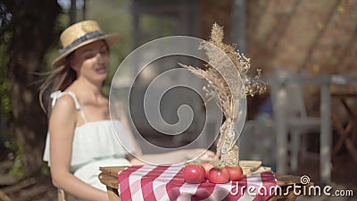 Jeune fille rurale sous un chapeau de paille et une longue robe blanche assise à la petite table avec des pommes et un vase déco banque de vidéos Jeune fille rurale sous un chapeau de paille et une longue robe blanche assise à la petite table avec des pommes et un vase déco banque de vidéos