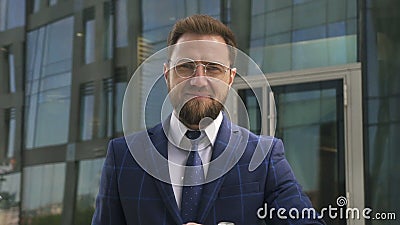Jeune homme d'affaires regardant la position de montre et de sourire sur le fond d'immeuble de bureaux banque de vidéos Jeune homme d'affaires regardant la position de montre et de sourire sur le fond d'immeuble de bureaux banque de vidéos