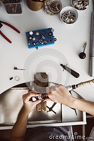 Jeweler`s workplace. Top view of jeweler`s workbenche with different tools on a white table. Female hands making a new Stock Photo