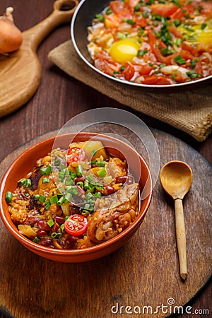 Jewish food hot cholent and fresh shakshuka in a frying pan on a set Shabbat table. Stock Photo