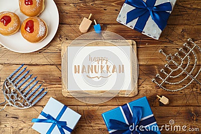 Jewish holiday Hanukkah greeting card with photo frame, traditional donuts, menorah and gift box on wooden background Stock Photo