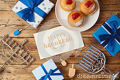 Jewish holiday Hanukkah greeting card with traditional donuts, menorah and gift box on wooden background Stock Photo