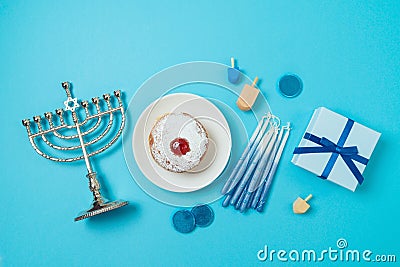 Jewish holiday Hanukkah top view composition with menorah, traditional donuts and gift box on blue background. Flat lay Stock Photo