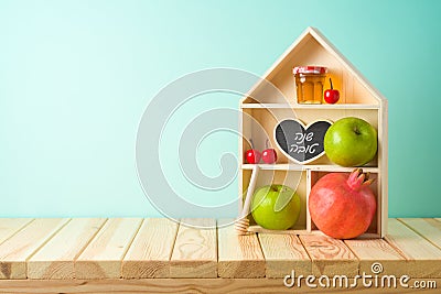 Jewish holiday Rosh Hashana creative decor background with toy house, honey jar, apple and pomegranate on wooden table Stock Photo