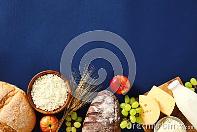 Jewish holiday Shavuot concept. Flat lay cottage cheese, bottle of milk, cereal bread, grape, apples, wheat on blue background Stock Photo