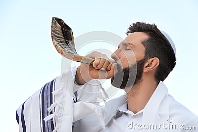 Jewish man in kippah and tallit blowing shofar outdoors. Rosh Hashanah celebration Stock Photo