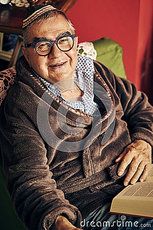 Jewish senior with glasses in the armchair reading a torah book Stock Photo