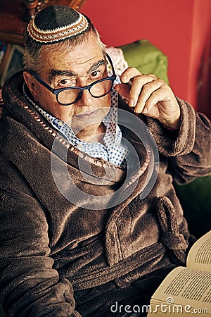 Jewish senior with glasses in the armchair reading a torah book Stock Photo