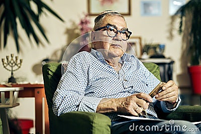 Pensive Jewish senior in the armchair reading a torah book Stock Photo