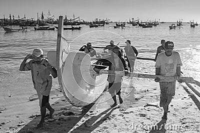 A team of fishermen carrying their fishing boat on shore after a day at sea Editorial Stock Photo