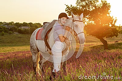 Jockey young girl petting and hugging white horse in evening sunset. Sun flare Stock Photo