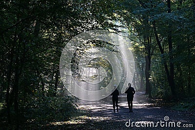 Jogging couple silhouetted against sunbeam in dark forest Stock Photo