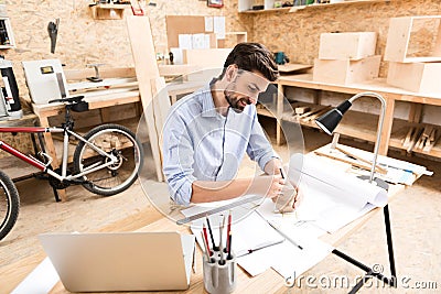 Jolly bearded woodworker drawing lines on timber item at table Stock Photo