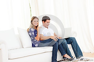 Jolly couple using a laptop sitting on sofa Stock Photo