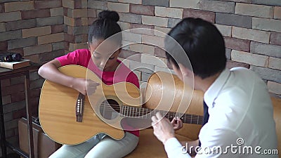 Jonge Aziatische mannelijke leraar die een gitaarles geven en onderwijzen hoe te gitaar aan Afrikaans Amerikaans meisje te spelen stock video Jonge Aziatische mannelijke leraar die een gitaarles geven en onderwijzen hoe te gitaar aan Afrikaans Amerikaans meisje te spelen stock video