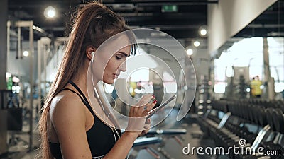 Jonge dichte omhooggaande portretvrouw die met oortelefoons aan muziek na harde training in gymnastiek luisteren Glimlachend aant stock video Jonge dichte omhooggaande portretvrouw die met oortelefoons aan muziek na harde training in gymnastiek luisteren Glimlachend aant stock video