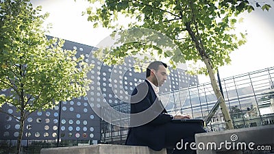 Jonge zakenmanzitting in een park dichtbij bureau en het gebruiken van laptop stock footage Jonge zakenmanzitting in een park dichtbij bureau en het gebruiken van laptop stock footage