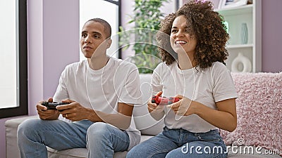 Joy-filled beautiful couple enjoy playing video game on their comfortable sofa, exuding confidence and happiness in the heart of Stock Photo