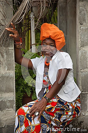 A joyful African-American woman wearing a bright colorful national dress is sitting in the opening of a brick gazebo Stock Photo