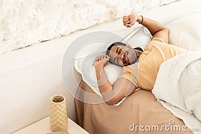 Joyful Arabic Man Awakening Stretching Arms Lying In Bedroom Indoors Stock Photo