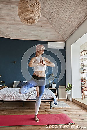 Joyful yoga practitioner in comfortable sportswear stands in tree position in light room Stock Photo