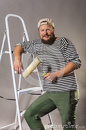 Joyful bearded craftsman with brush roller and ladder Stock Photo