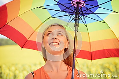 Joyful beautiful girl holding multicolored umbrella in sunflower field and blue cloud sky background Stock Photo