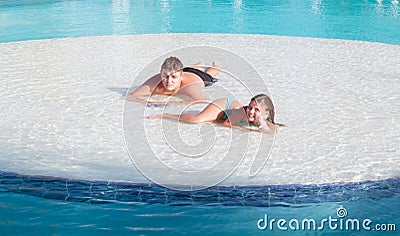 Joyful beautiful smiling little girl and teenage boy relaxing in swimming pool island on summer beautiful gorgeous day Stock Photo