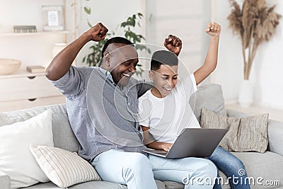 Joyful black granddad and grandson watching sports on laptop and emotionally cheering Stock Photo