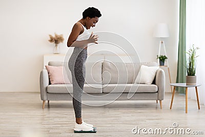 Joyful Black Lady Weighing Standing On Weight-Scales At Home Stock Photo