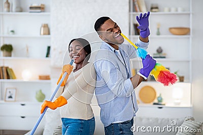 Joyful black man and his girlfriend singing during housecleaning, using mop and duster as microphones Stock Photo