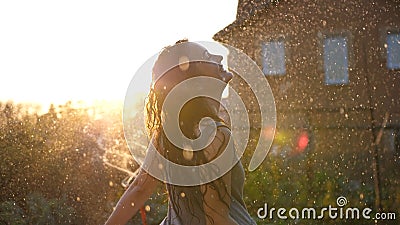 Joyful brunette girl enjoys her evening in the countryside by dancing in the rain. Stunning golden sun rays shine on Stock Photo