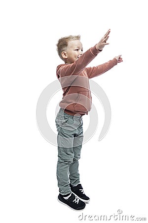 The joyful boy raised his hands up. A blond guy in a brown hoodie and gray trousers. Positivity and happiness. Isolated on white Stock Photo