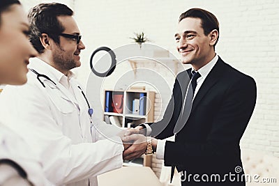 Joyful businessman shaking hands with doctor who cured ailment. Acknowledgments. Stock Photo