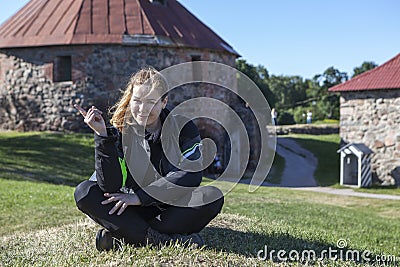 Joyful Caucasian woman in motorcycle jacket, knee guards sitting on green meadow in some landmark, copyspace Stock Photo